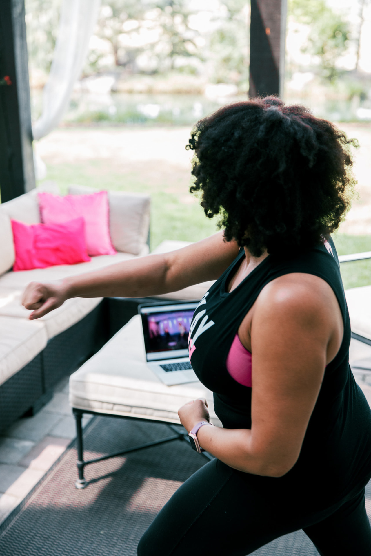 A woman dancing along to a SHiNE Online class on her laptop outdoors