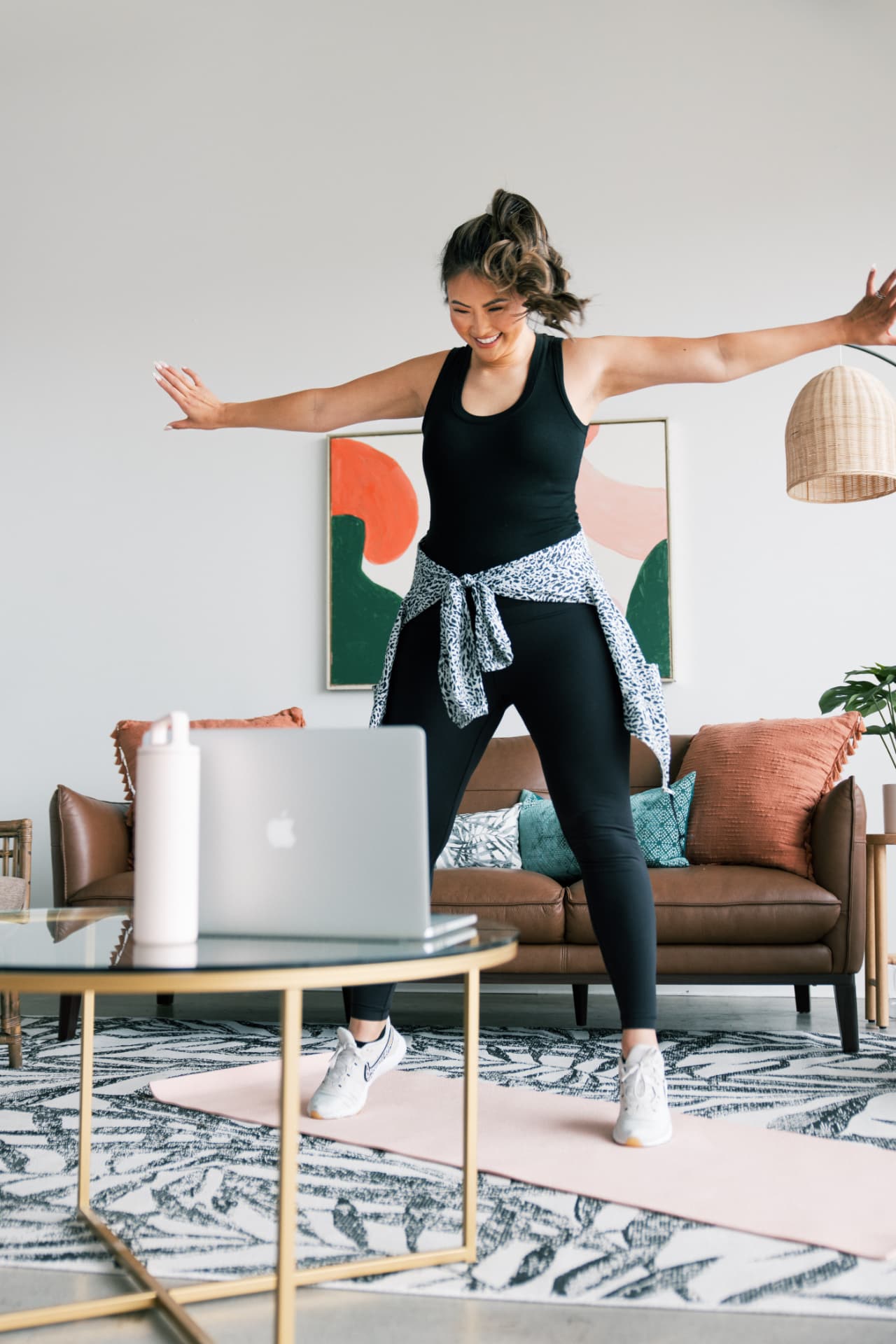 A smiling woman dancing along with a SHiNE Online class on her laptop in her living room